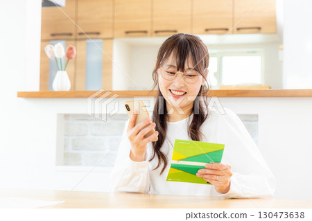 A woman using a smartphone and a household account book 130473638
