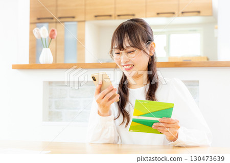 A woman using a smartphone and a household account book 130473639