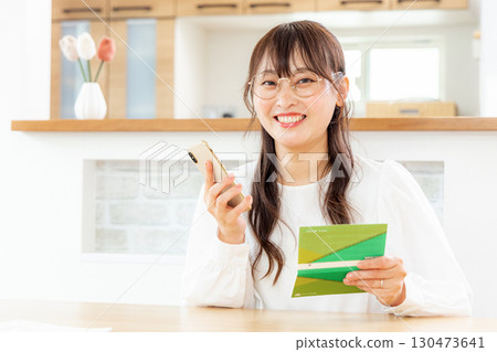 A woman using a smartphone and a household account book 130473641