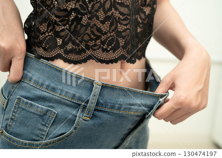 Young Asian woman losing weight wearing loose pants in oversize jeans. Young Asian woman losing weight wearing loose pants in oversize jeans. 130474197
