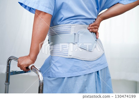 Asian senior pain back wearing elastic support belt with walker. 130474199