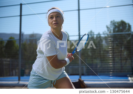 Focused Female Tennis Player Holding Racket on Outdoor Court 130475644