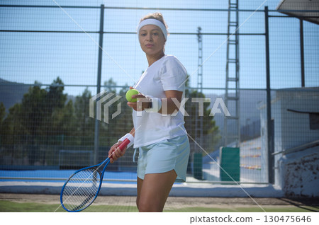 Focused Tennis Player Holding Ball on Court in Sunlit Outdoor Setting 130475646