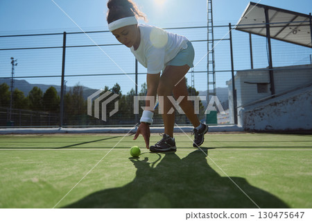 Woman in Sportswear Picking Up Tennis Ball on Outdoor Court 130475647