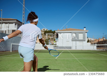 Female Athlete Playing Tennis on an Outdoor Court in Bright Daylight 130475660