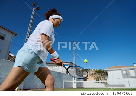 Woman Playing Tennis Outdoors on a Clear Sunny Day Woman Playing Tennis Outdoors on a Clear Sunny Day 130475665