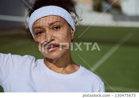 Young Woman Standing by Tennis Court Wearing Headband and Sport Outfit Young Woman Standing by Tennis Court Wearing Headband and Sport Outfit 130475673