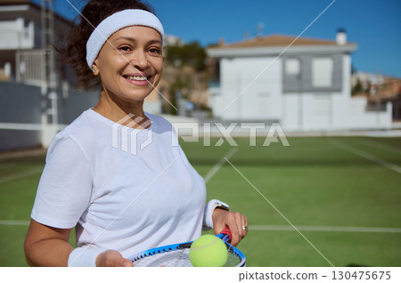 Smiling Woman Posing on Outdoor Tennis Court in Daylight with Racket and Ball Smiling Woman Posing on Outdoor Tennis Court in Daylight with Racket and Ball 130475675