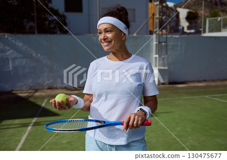 Active Woman Smiling on a Tennis Court Holding Racket and Ball Active Woman Smiling on a Tennis Court Holding Racket and Ball 130475677