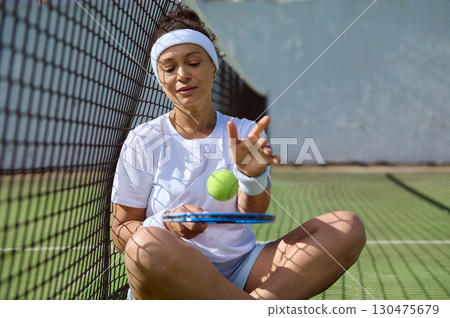 Woman Sitting on Tennis Court With Tennis Ball and Racket Relaxing Woman Sitting on Tennis Court With Tennis Ball and Racket Relaxing 130475679