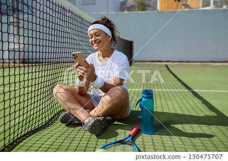 Woman Relaxing on Tennis Court Using Smartphone After a Match 130475707
