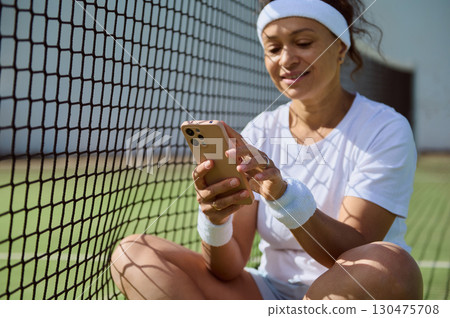 Woman Relaxing on Tennis Court Using Smartphone After Training 130475708