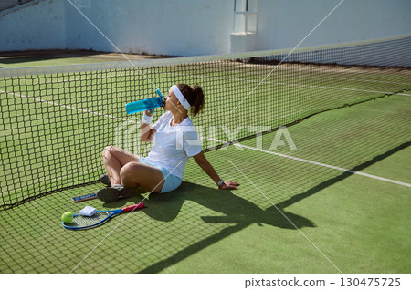 Female Tennis Player Resting by the Net on a Sunny Court 130475725