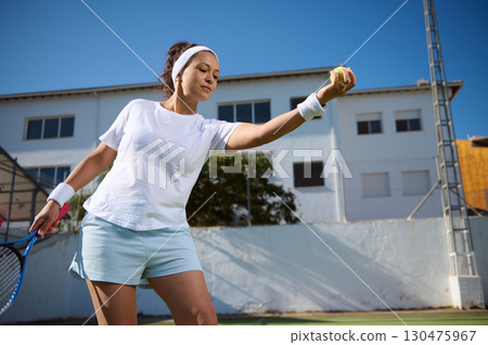 Woman Playing Outdoor Tennis Focused on Serving the Ball 130475967