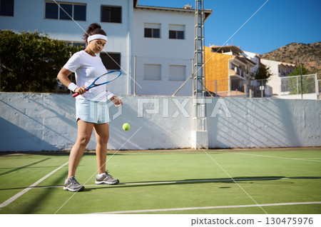 Woman Practicing Tennis with Racket on Sunny Outdoor Court Woman Practicing Tennis with Racket on Sunny Outdoor Court 130475976