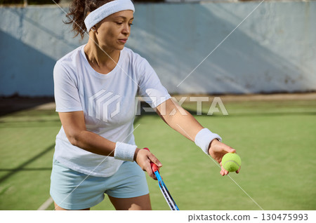 Woman Practicing Tennis Serve on Sunny Outdoor Court in Sports Attire 130475993