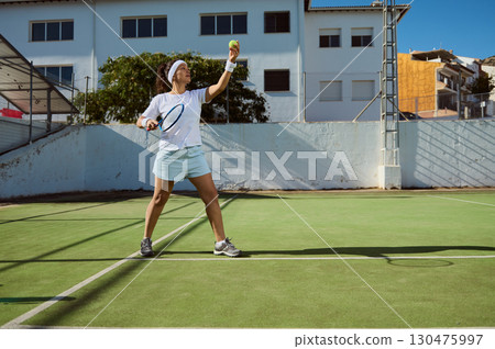 Female Tennis Player Preparing to Serve on Sunny Outdoor Court Female Tennis Player Preparing to Serve on Sunny Outdoor Court 130475997