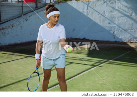 Woman Preparing to Serve Tennis Ball on Outdoor Court 130476008
