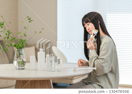 Smiling Asian woman using a facial beauty device for home beauty treatment, lifting, and massage (worried, worried, troubled) 130476508