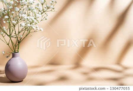 Delicate white gypsophila flowers in a lilac vase on a pastel beige background with sunny shadows. Delicate white gypsophila flowers in a lilac vase on a pastel beige background with sunny shadows. 130477055