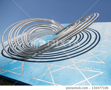 Contemporary metal sculpture on a vibrant blue wall in an urban outdoor setting under clear skies Contemporary metal sculpture on a vibrant blue wall in an urban outdoor setting under clear skies 130477106