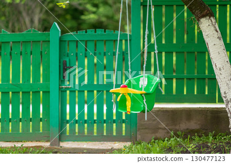 Colorful swing in a backyard near a green wooden fence with a scenic garden view 130477123