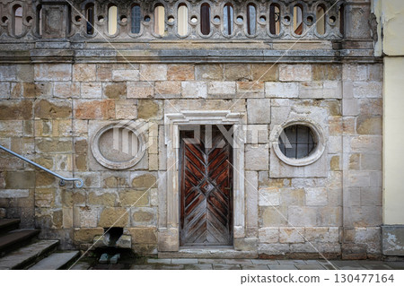 Old architectural structure featuring a wooden door and stone wall in a historical urban setting Old architectural structure featuring a wooden door and stone wall in a historical urban setting 130477164