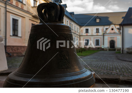 Historic bell stands in courtyard of old monastery at sunset, highlighting intricate details and atmosphere Historic bell stands in courtyard of old monastery at sunset, highlighting intricate details and atmosphere 130477190