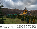 Wooden cottage surrounded by evergreen trees in a serene landscape during overcast weather 130477192