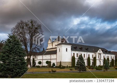 Wooden cottage surrounded by evergreen trees in a serene landscape during overcast weather 130477194