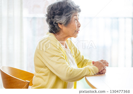 Senior woman sitting on a chair at a table Senior woman sitting on a chair at a table 130477368