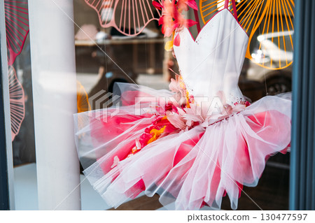 Pink and white ballerina tutu dress adorned with artificial flowers and tulle in a boutique display window. Costume craftsmanship, childhood fantasy, performative identity, theatrical design 130477597