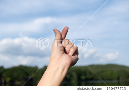 Close-up Hand Making Finger Heart Symbol Against Sky and Clouds Close-up Hand Making Finger Heart Symbol Against Sky and Clouds 130477723