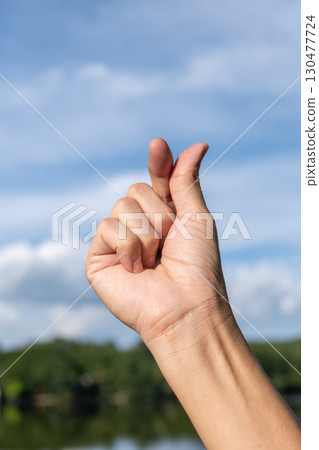 Hand Showing Korean Finger Heart Gesture with Blue Sky Background 130477724