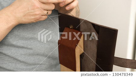 Leather artisan sewing brown wallet on wooden stitching pony with needle and thread Leather artisan sewing brown wallet on wooden stitching pony with needle and thread 130478349