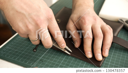 Leather artisan using divider tool to mark stitching line on brown leather wallet closeup Leather artisan using divider tool to mark stitching line on brown leather wallet closeup 130478357