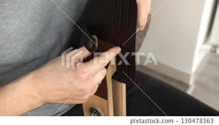 Leatherworker hand stitching rough leather piece with needle and thread on wooden clamp closeup Leatherworker hand stitching rough leather piece with needle and thread on wooden clamp closeup 130478363