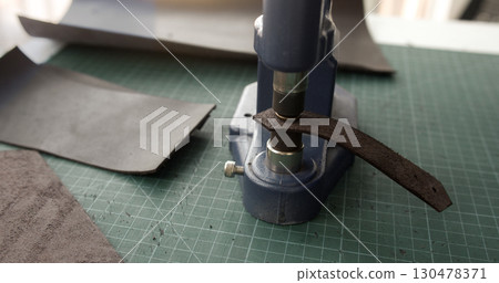 Close up of leather strap placed under press machine in workshop for handmade accessory production Close up of leather strap placed under press machine in workshop for handmade accessory production 130478371