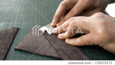 Leatherworker skiving edge of brown leather piece with blade tool on green cutting mat closeup Leatherworker skiving edge of brown leather piece with blade tool on green cutting mat closeup 130478375