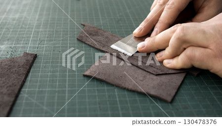 Leatherworker skiving leather piece with blade tool on green cutting mat Leatherworker skiving leather piece with blade tool on green cutting mat 130478376