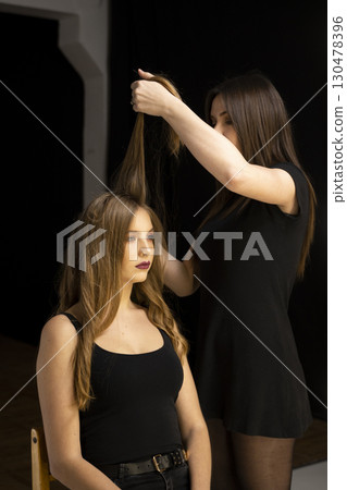 Hairdresser styling long hair of young woman with curls in beauty studio 130478396