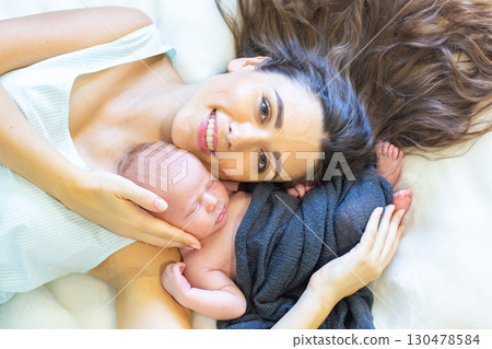 Mother cuddling newborn baby on soft bedding in cozy indoor space during daylight hours Mother cuddling newborn baby on soft bedding in cozy indoor space during daylight hours 130478584