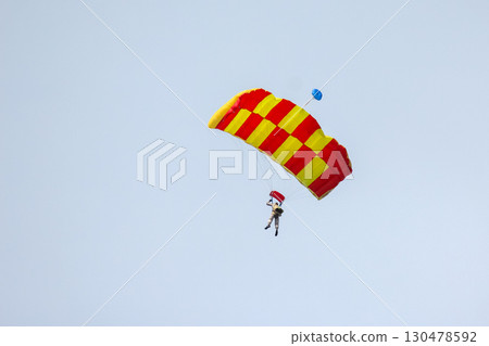 Skydiver descends with colorful parachute over open sky during bright daylight 130478592
