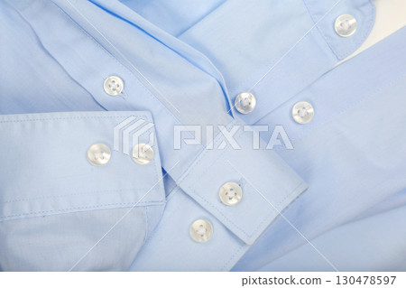 Close-up view of light blue shirt fabric with buttons showing intricate detail and texture 130478597