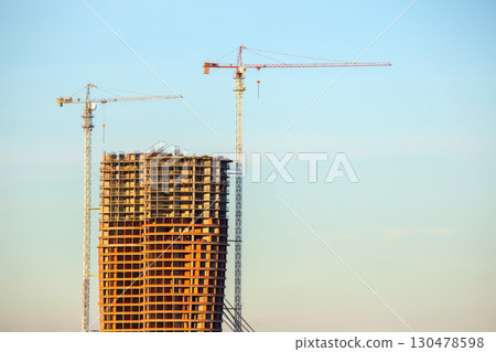 Construction of a high-rise building with cranes against a clear blue sky 130478598