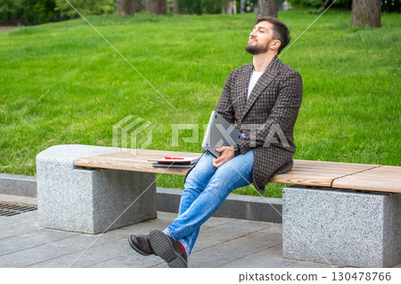 Man enjoying a moment of relaxation in a park while holding a laptop Man enjoying a moment of relaxation in a park while holding a laptop 130478766
