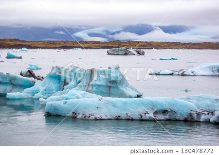 Glacial icebergs float in a serene lake in Iceland during overcast weather 130478772
