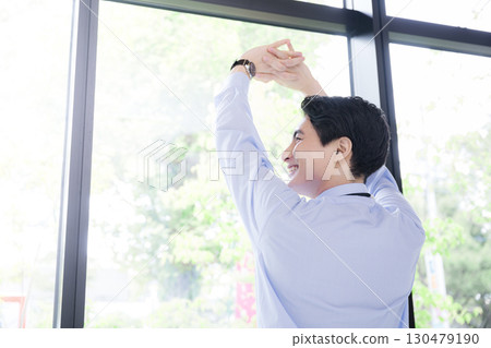 A refreshing businessman taking a break and stretching by the window A refreshing businessman taking a break and stretching by the window 130479190