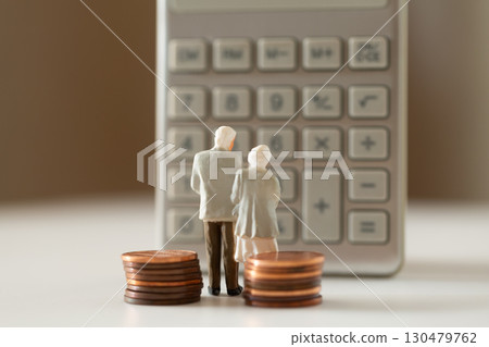 A miniature elderly couple and coins standing in front of a calculator. Pension. Retirement money image. 130479762