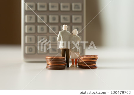 A miniature elderly couple and coins standing in front of a calculator. Pension. Retirement money image. 130479763